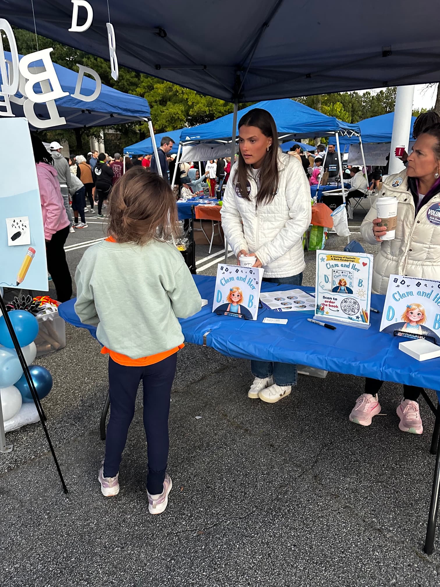 A girl visits a book stall for "Clara and Her D's and B's" outdoors.