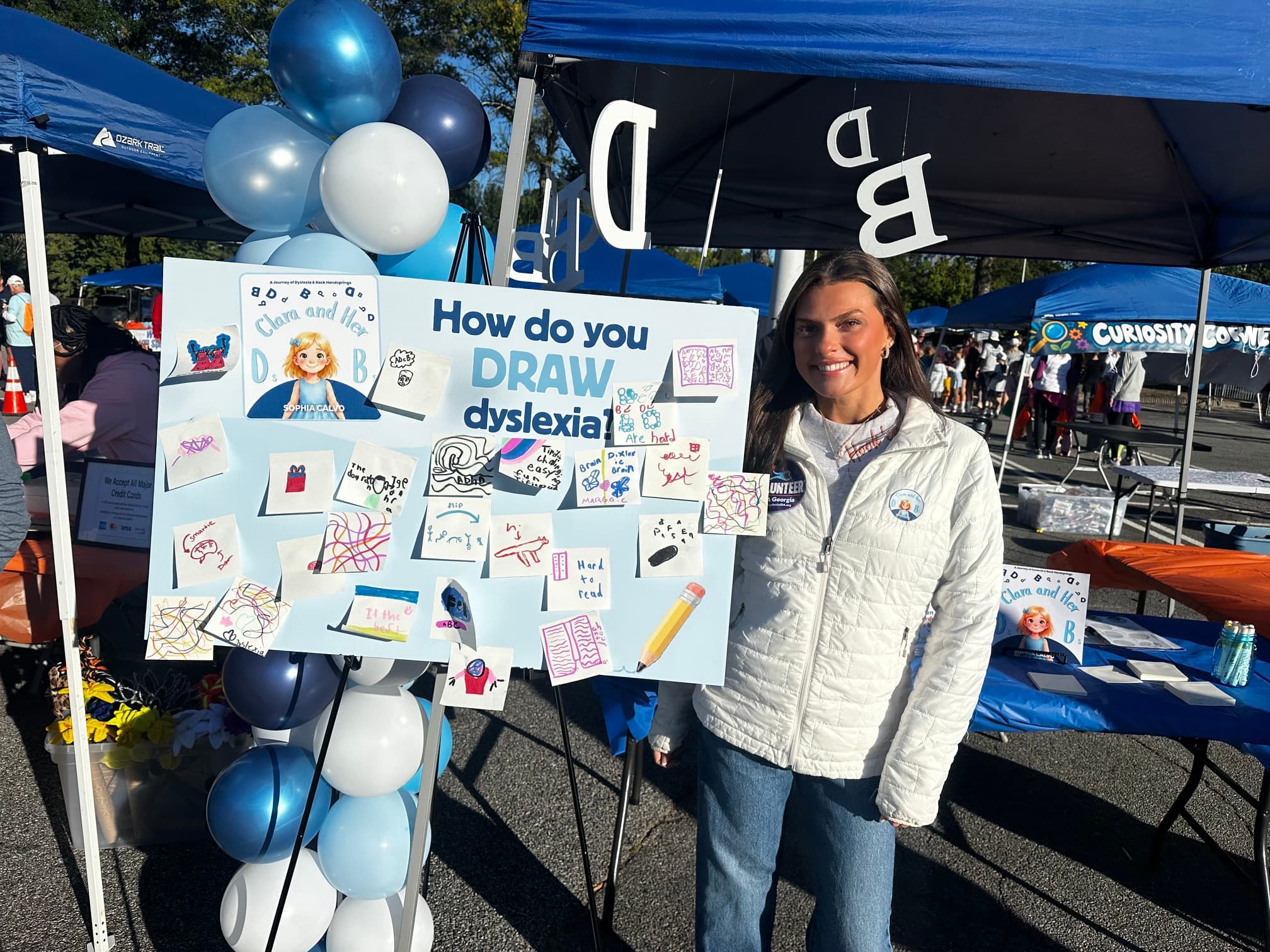 Woman smiles next to a dyslexia awareness poster covered in colorful sticky note drawings.