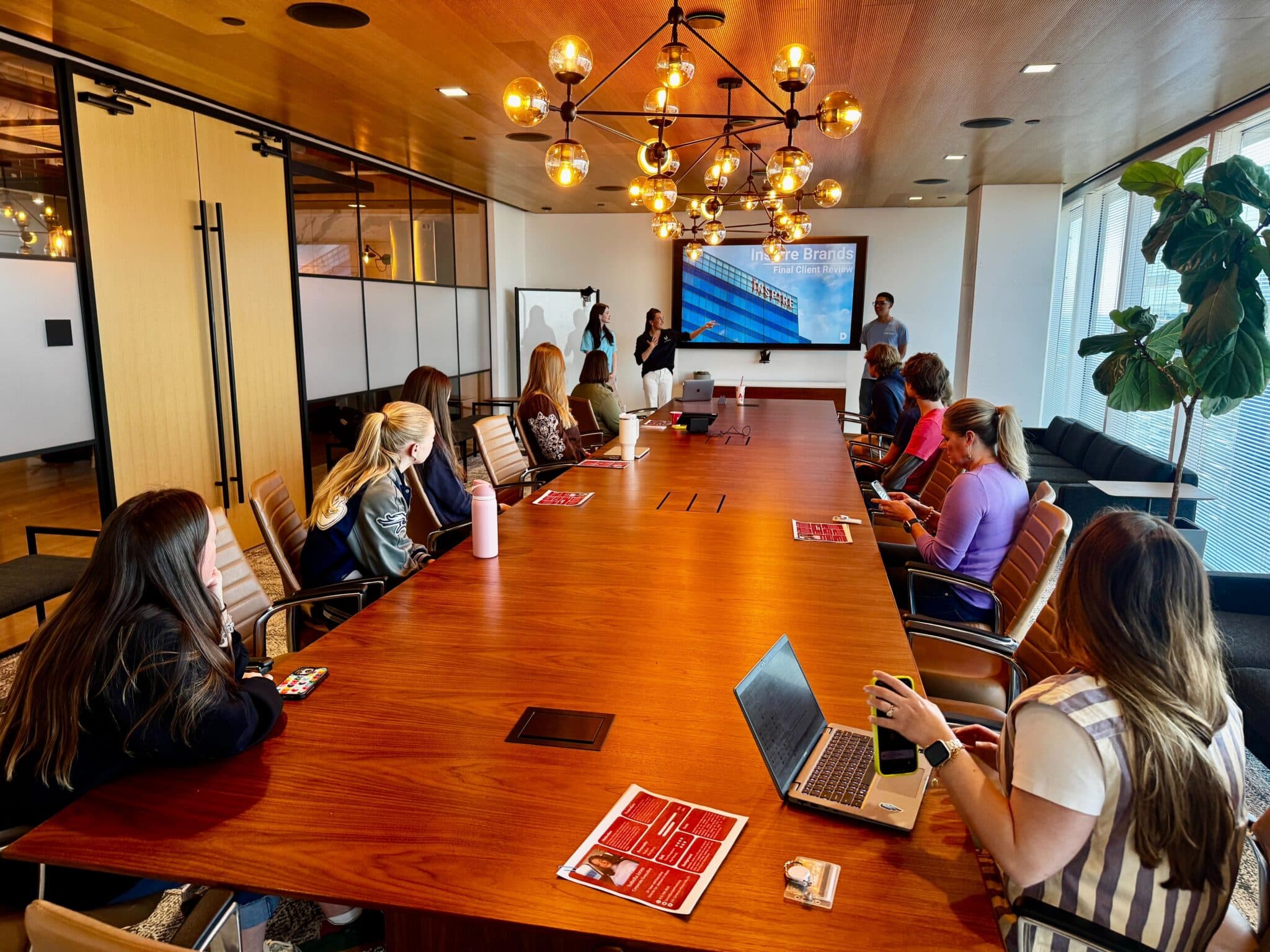 People watch an Inspire Brands presentation while seated at a long wooden conference table.
